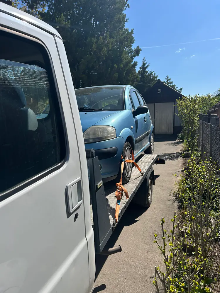 Világoskék Citroën C2 szállítása NV trélerrel napsütésben