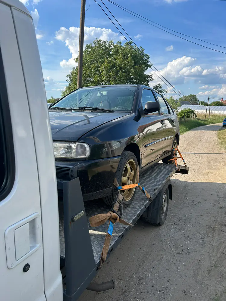 Fekete hatchback szállítása NV Autómentő trélerrel napsütésben