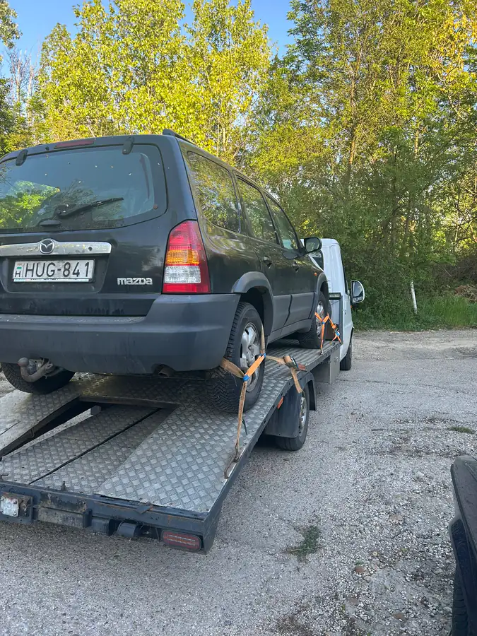 Fekete Mazda Tribute terepjáró szállítása NV trélerrel, erdei úton